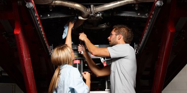 Two mechanics working together under a lifted car on a vehicle lift.
