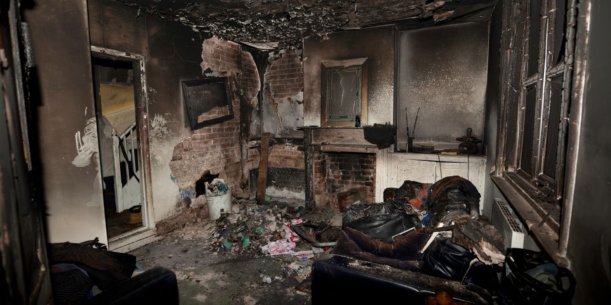 A living room severely damaged by fire, with charred walls and debris scattered.