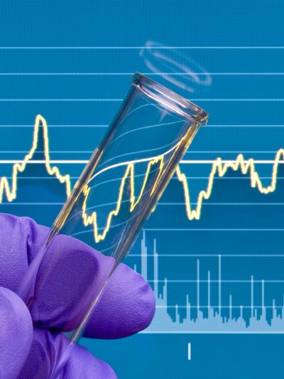 Hand with purple glove holding a test tube with financial graph reflected.