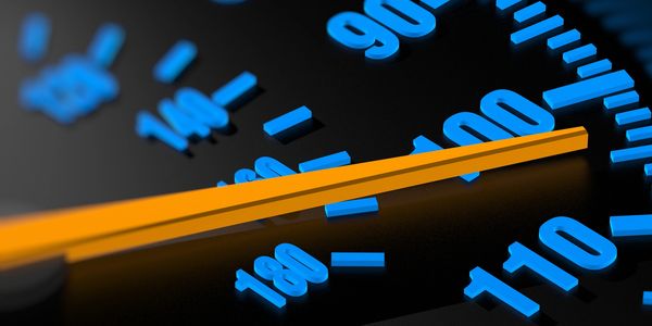 Close-up of a speedometer needle pointing near 100 with blue numbers.