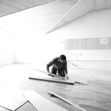 Person installing wooden flooring in a bright room.