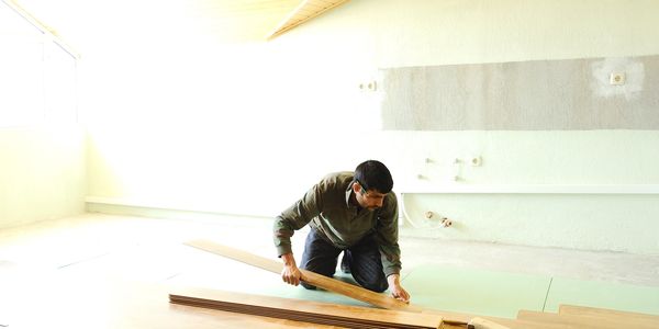 Man installing wooden flooring in a bright room.