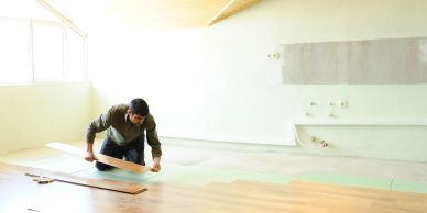 Man installing wooden flooring in a bright, empty room.