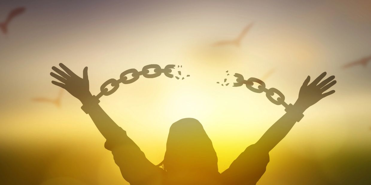 Silhouette breaking free from chains against sunset.