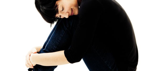 Young woman in black hugging her knees with a serene smile.