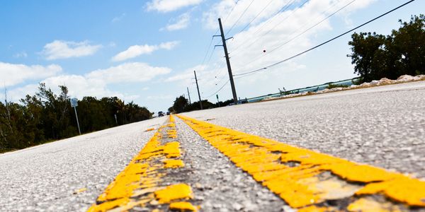 Close-up of a yellow road line on a sunny day with clear blue sky.