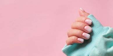 Hand with pastel pink ombre nails against a pink background.
