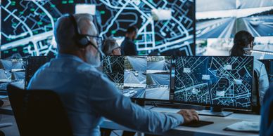 Man monitoring multiple screens with maps in a control room.