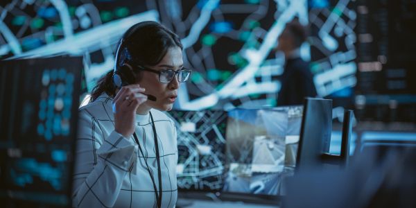Woman in headset monitoring control room screens.
