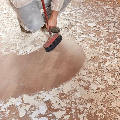 Person in protective suit sweeping chipped paint off wooden floor.