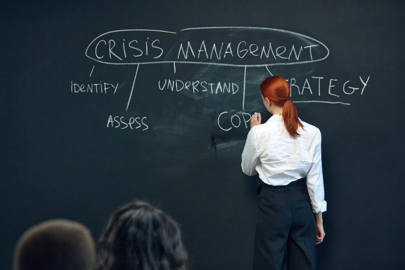 Young woman writing on blackboard plan of crisis management during team meeting.