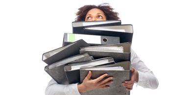 A person struggling to carry a large stack of binders and folders.