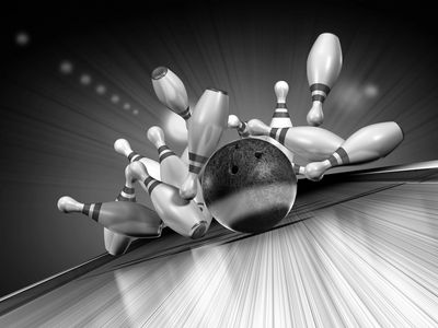 Bowling ball striking pins in a dramatic black and white action shot.