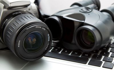 Camera lens and binoculars placed on a laptop keyboard.
