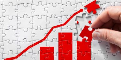 Hand placing puzzle piece on rising bar chart.