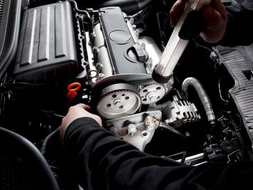 Mechanic inspecting and working on a car engine's timing belt.