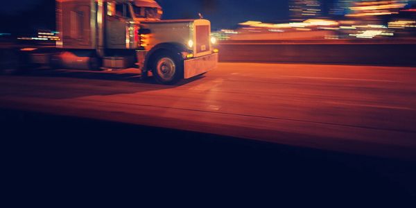 A semi truck driving fast on a city road at night.