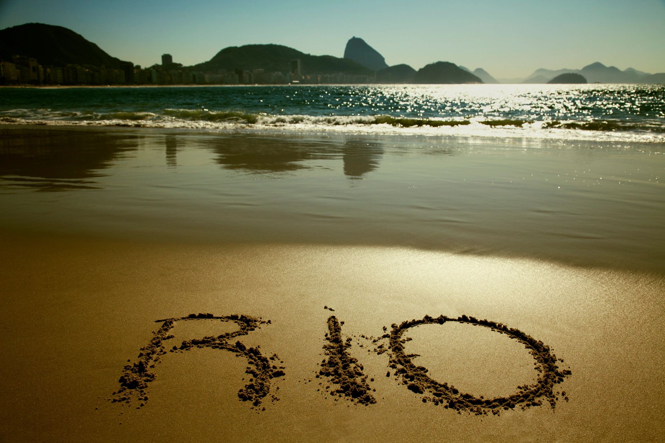 Praia com a palavra "RIO" escrita na areia.