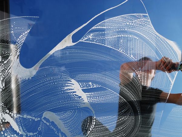 Person cleaning a window with a squeegee on a sunny day.