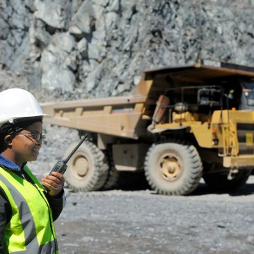 Safety officer using a walkie-talkie at a mining site with heavy machinery.