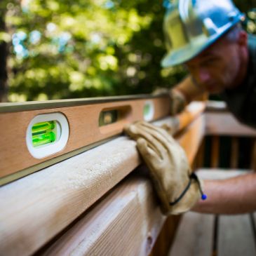 Construction worker using a level to check wood alignment outdoors.
