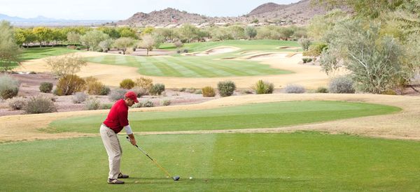 Golfer in red shirt preparing to tee off on a sunny golf course.