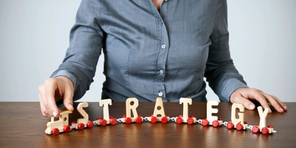 Person arranging wooden letters on a toy train spelling 'STRATEGY'.
