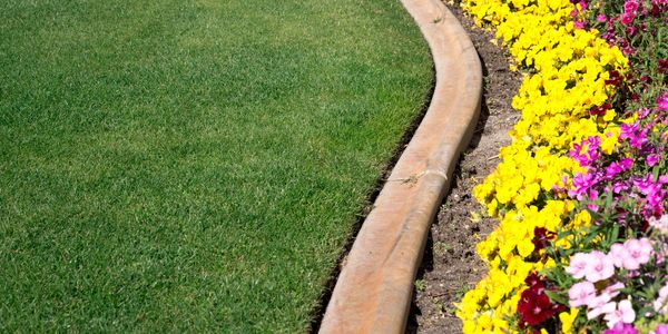 Green lawn next to vibrant flower bed with stone border.