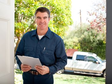 A delivery man in blue uniform holding a clipboard at a doorway.