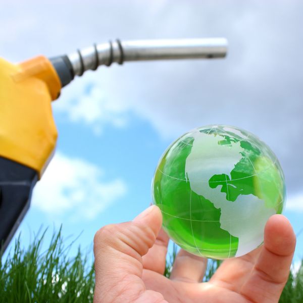 A hand holding a green glass globe near a yellow fuel pump nozzle.