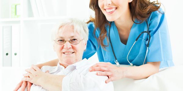 Smiling nurse supporting an elderly woman in a bright room.