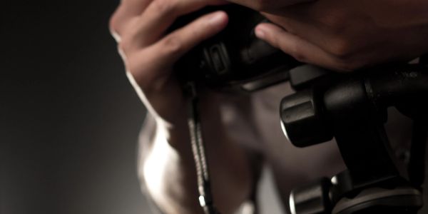 Close-up of hands adjusting a camera on a tripod in dim lighting.