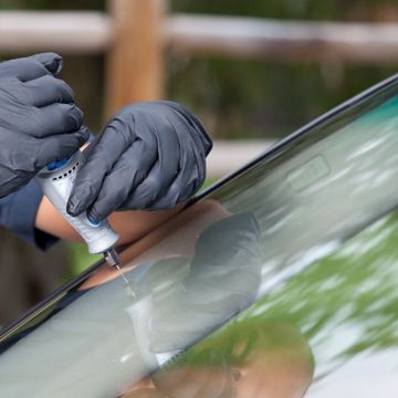 Person repairing car windshield with a tool.