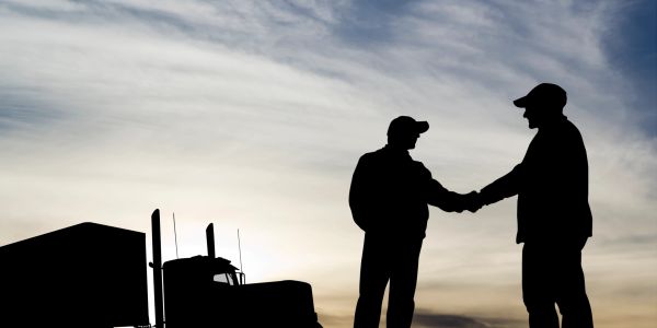 Two men shaking hands near a truck at sunset.