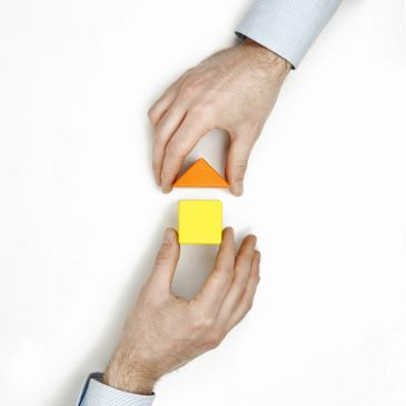 Hands holding colorful wooden blocks, forming a shape.