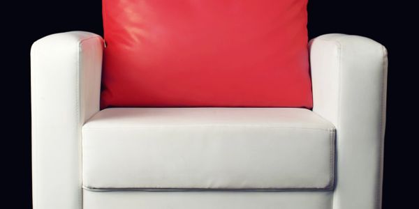 Modern white armchair with a vibrant red cushion on a black background.