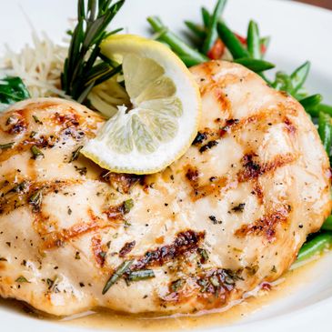 Grilled chicken breast garnished with lemon and herbs, served with vegetables.