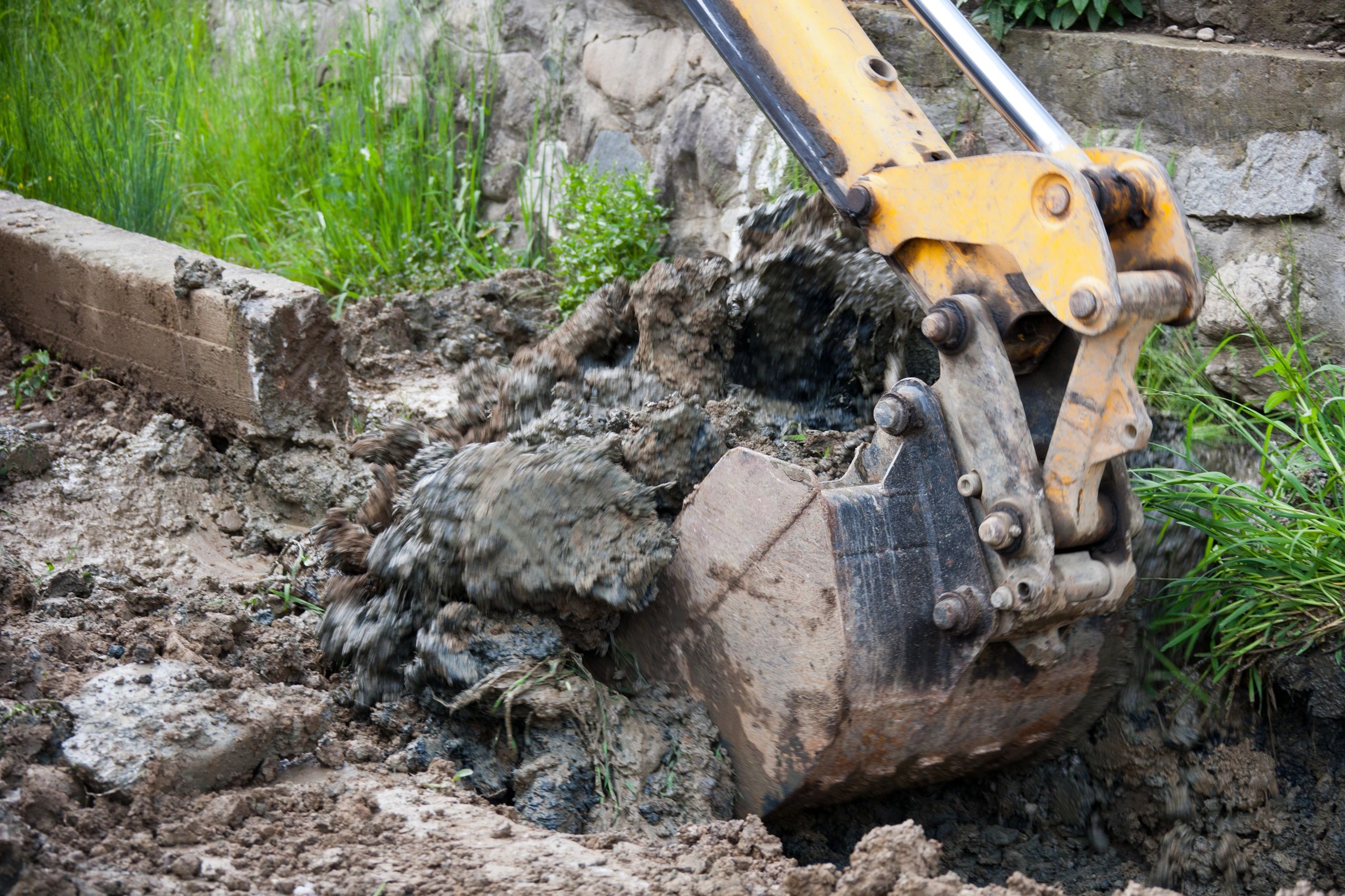 Yellow excavator digging a trench in a forest clearing.