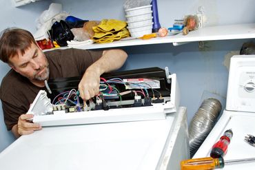 A man repairs a washing machine with tools nearby.