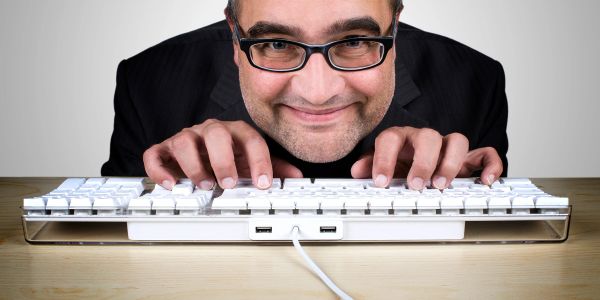 Man with glasses typing eagerly on a keyboard.