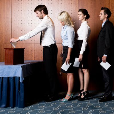 People in formal attire standing in line to cast votes in a ballot box.