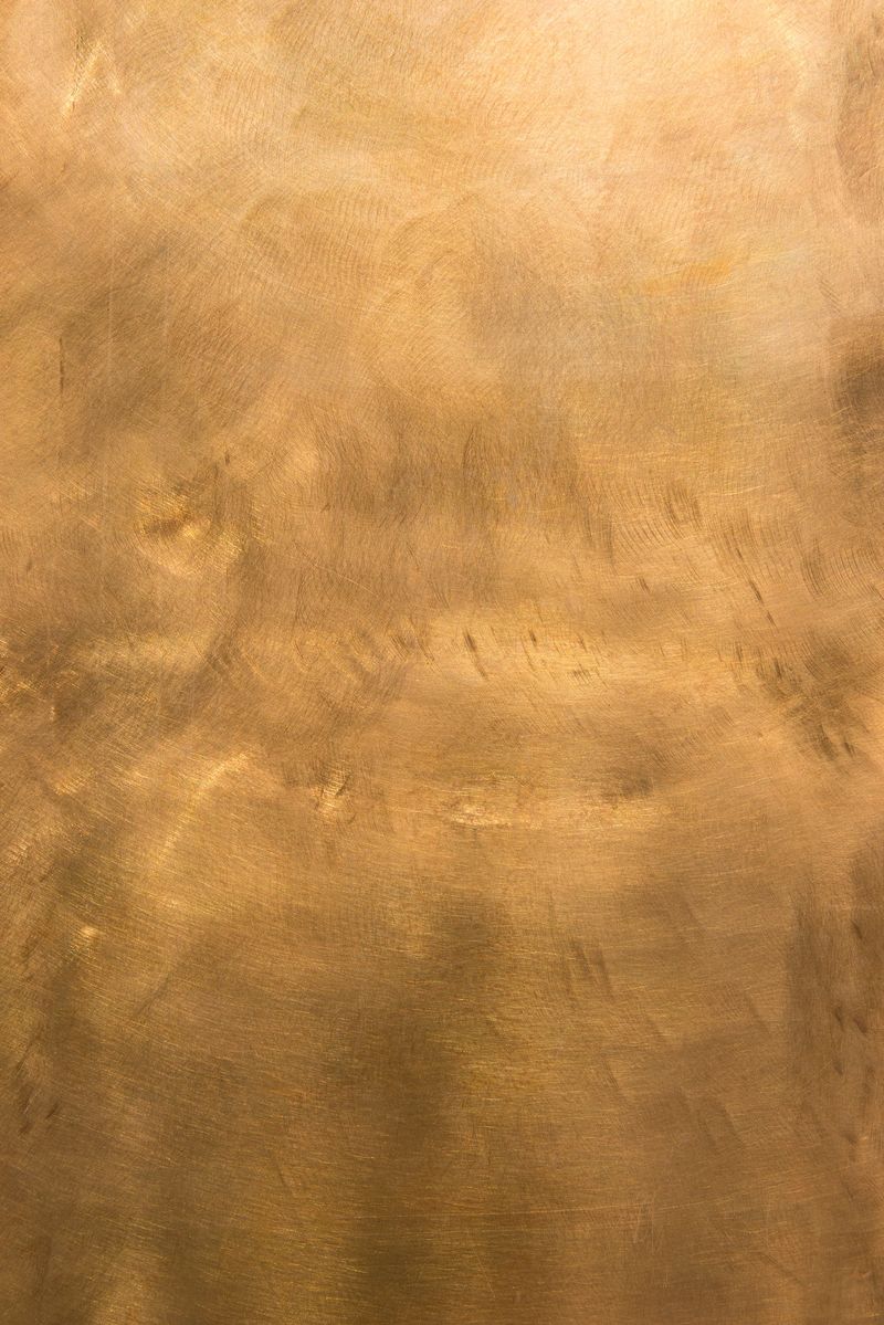 Brushed brown-golden copper or bronze surface, with visible brush strokes. The sheet metal has an appealing cloudy, wavy texture. Vertical orientation. The image has been shot outdoors during natural day light, full frame and close up. Ideal for backgrounds. The size of the photo is 4912 x 7360 px. High resolution.