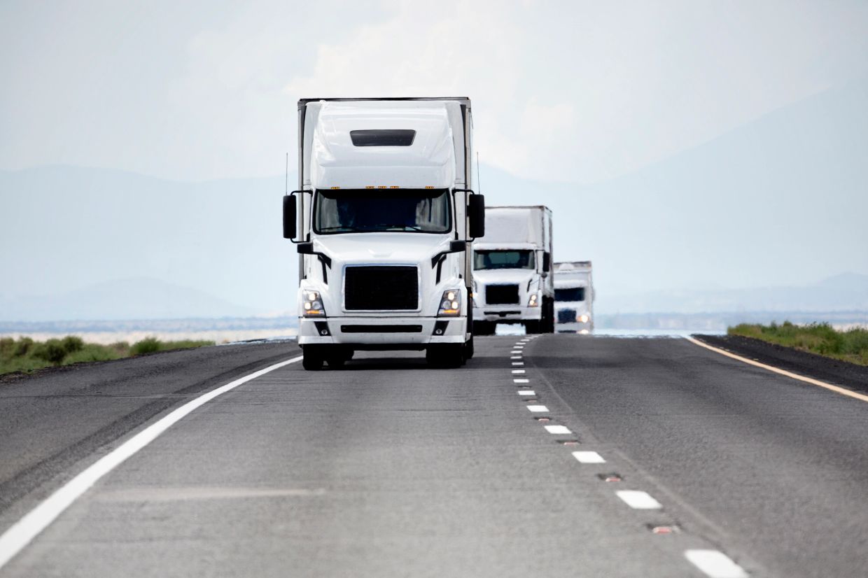 Three white semi-trucks driving on a highway.