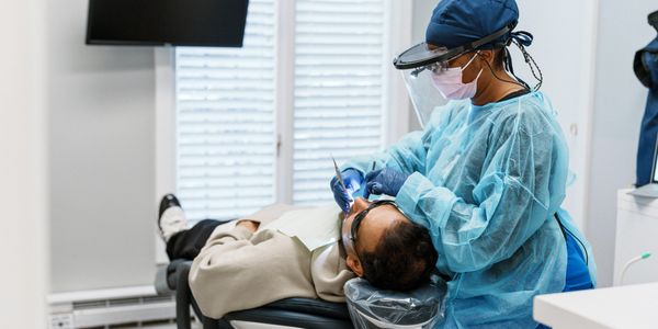 A dental hygienist wearing full PPE performs scaling on a patient who is lying on a reclined dental 