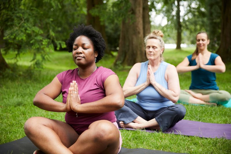 Group of four women doing yoga exercises in the morning in the sunshine in the city park with a yoga teacher and have fun