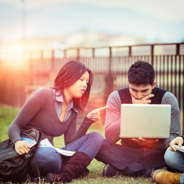 Two students studying together outdoors using a laptop.