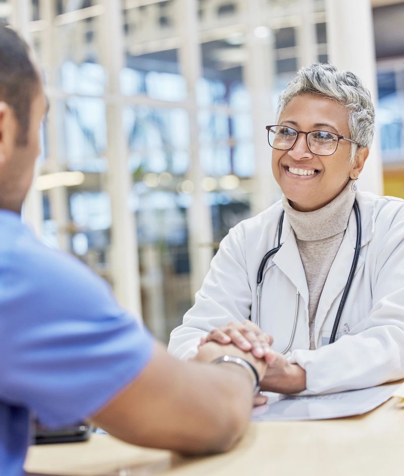 Smile, support and doctor holding hands with patient at consultation for healthcare and empathy in office. Happy woman, man and helping hand in medicine, trust and comfort in medical care at hospital