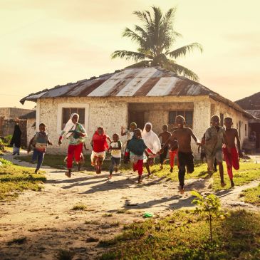 Niños corriendo y jugando frente a una casa rústica.