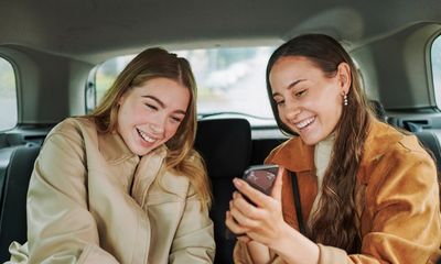 Two women happily looking at a phone inside a car.