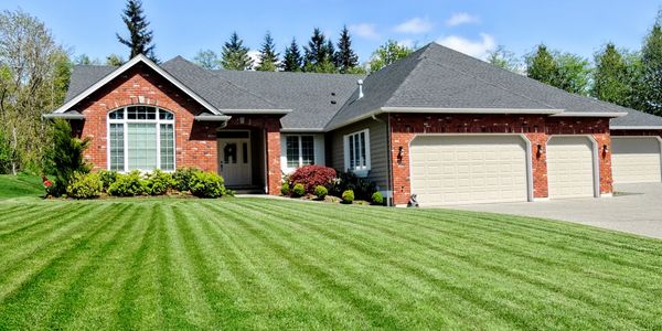A brick house with a neatly mowed striped lawn under a blue sky.